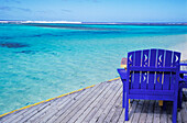 Leerer blau gestrichener Stuhl auf Holzdeck am Meer
