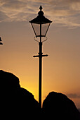 Silhouette eines Laternenpfahls und eines Felsens bei Sonnenuntergang; Lee, North Devon, England