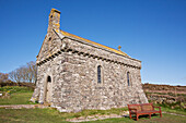 An old stone church with a bench and blue sky