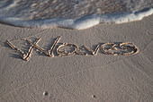 Das Wort Waves handgeschrieben im Sand am Rande des Wassers; Tulum, Mexiko