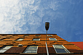 Niedriger Blickwinkel auf ein Backsteingebäude und eine Straßenlaterne mit blauem Himmel und Wolken; London, England