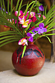 Ein Blumenarrangement in einer kleinen roten Vase; Ulpotha, Embogama, Sri Lanka