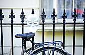 Bike Leaning Against A Metal Fence With A White Mask, Notting Hill; London, England