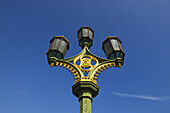 Niedriger Blickwinkel auf einen verzierten Laternenpfahl vor blauem Himmel; London, England