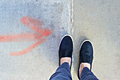 Ein roter Pfeil, der auf den Beton gesprüht wurde und zu den Füßen zeigt; London, England