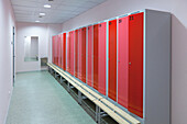Sports and exercise facilities indoors. Gym. Changing room, locker room. Red cupboard doors. Bench seat.