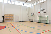 Indoor basketball court at a school. Wooden floor and marked court, a hoop and backboard.