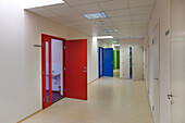 A school corridor with coloured doors opening off it. Red, blue and green doors. Lockers and cupboards.