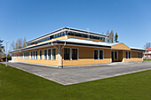 The exterior of a modern school building, single storey building with windows and a playground area and grass. 