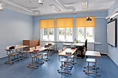 Ein Klassenzimmer in einer Schule mit Tischen und Stühlen und gelben Jalousien.