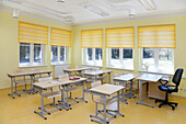 Ein Schulklassenzimmer mit Tischen und Stühlen und gelben Fensterläden.