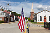 Die amerikanische Flagge weht auf einer ruhigen Hauptstraße mit Häusern und einer Kirche. 