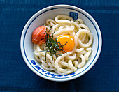 A dish of noodles, vegetables and fish with a yellow egg yolk. 