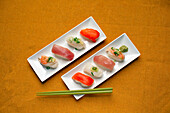 Sushi-Platte, eine Auswahl an rohem Fisch und Reissnacks mit Essstäbchen. 