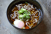 A black china bowl of noodles and broth with sliced chillis and an egg.