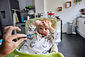 Kleinkind mit erhobenen Händen, das im Hochstuhl sitzend in der Küche das Essen verweigert