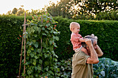 Großvater trägt Kleinkind auf den Schultern beim Spaziergang im Garten