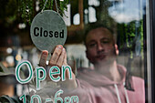 Man placing Closed sign in window of shop