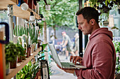 Mann macht Bestandsaufnahme mit Laptop in einem Blumenladen