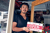 Mann hängt ein Schild mit der Aufschrift Open an einer Restauranttür auf. Zweisprachig, italienisch und englisch. 