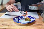 Ein Mann bei der Zubereitung von Speisen in einer Restaurantküche, der mit einer Zange Gemüse auf einen Teller legt. Nahaufnahme.