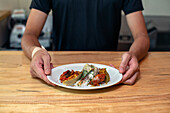 Ein Mann, der an einer Restauranttheke steht und Teller mit gekochtem Essen präsentiert, Menügerichte.