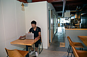 A man seated at a table using a laptop computer, owner and manager of a small restaurant. 
