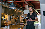 Ein Mann, der in einem Restaurant an einer offenen Küche arbeitet, mit Weinflaschen in der Hand. 