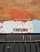 An old PARKING sign on a building wall. 