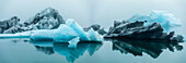 Europa, Island. Morgennebel dämpft das Licht auf Eisbergen, die in der Gletscherlagune Jokulsarlon an der Südküste schwimmen.