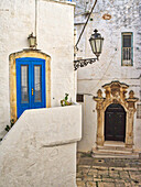 Italien, Apulien, Brindisi, Itria-Tal, Ostuni. Eine blaue Tür und kunstvolle Schnitzereien umgeben einen anderen Eingang.