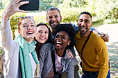 Smiling woman taking selfie with smart phone while standing with friends in park