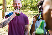 Young friends drinking beer while standing in park