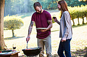 Smiling young couple talking while standing near barbecue grill in park