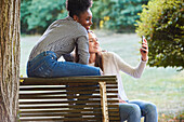 Smiling young friends talking selfie on smartphone in public park