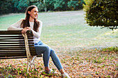 Lächelnde junge Frau auf einer Bank im Park sitzend