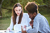Young female friends studying at table in park