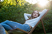 Thoughtful young woman with hands behind head leaning on chair