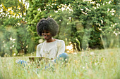 Lächelnde junge Frau, die ein digitales Tablet in einem öffentlichen Park benutzt