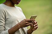 Mittelteil einer jungen Frau, die ein Smartphone im Park benutzt