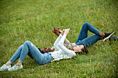 Young female friends lying on grass while using smart phone in park