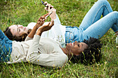 Junge Freundinnen liegen im Gras und benutzen ihr Smartphone in einem Park