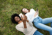 Junge Freundinnen liegen im Gras und benutzen ihr Smartphone im Park