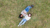 Junge Freundinnen liegen im Gras und benutzen ihr Smartphone in einem Park, Orgeval