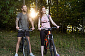 Lächelndes junges Paar steht mit Fahrrädern im Wald