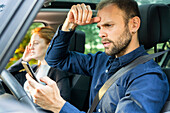 Frustrierter junger Mann, der sein Smartphone am Steuer eines Autos benutzt