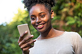 Nahaufnahme einer lächelnden jungen Frau, die ein Smartphone im Park benutzt
