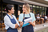 Mittelaufnahme von zwei Restaurantbesitzerinnen, die vor ihrem Restaurant eine Liste prüfen