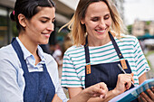 Two successful female entrepreneurs checking a list in front of their restaurant