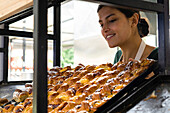 Medium shot of a female Latin-American bakery owner looking at her pastries displayed on a shelf
